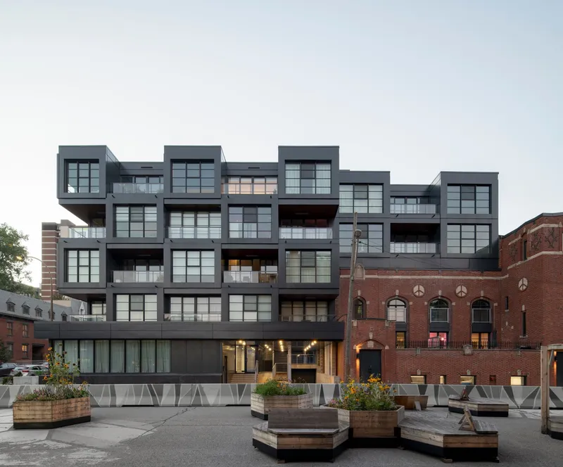Ground-level plaza with hexagonal planters and seating facing the cantilevered facade at twilight