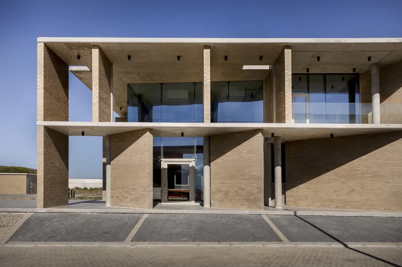 Two-story facade with buff brick columns and exposed concrete beams framing glazed openings under clear sky