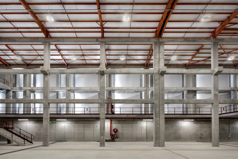 Interior hall with exposed concrete columns and red steel roof structure over mezzanine levels
