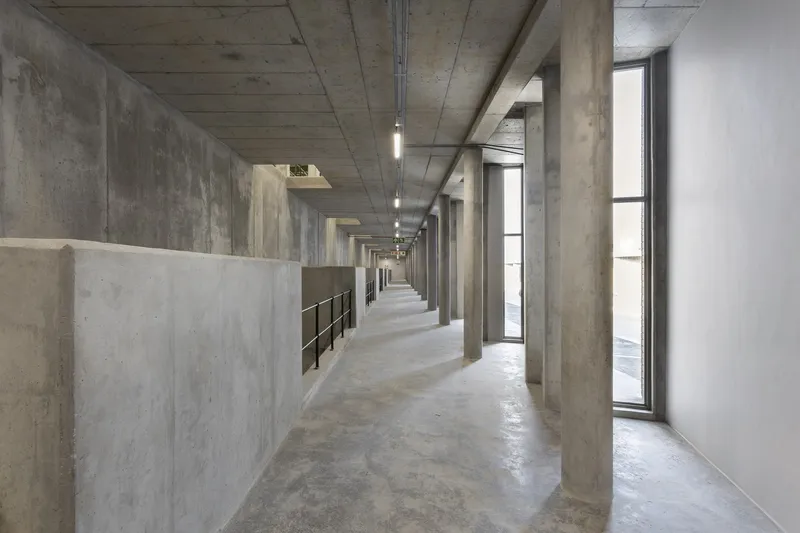 Concrete corridor with board-formed ceiling and tall narrow windows along one side