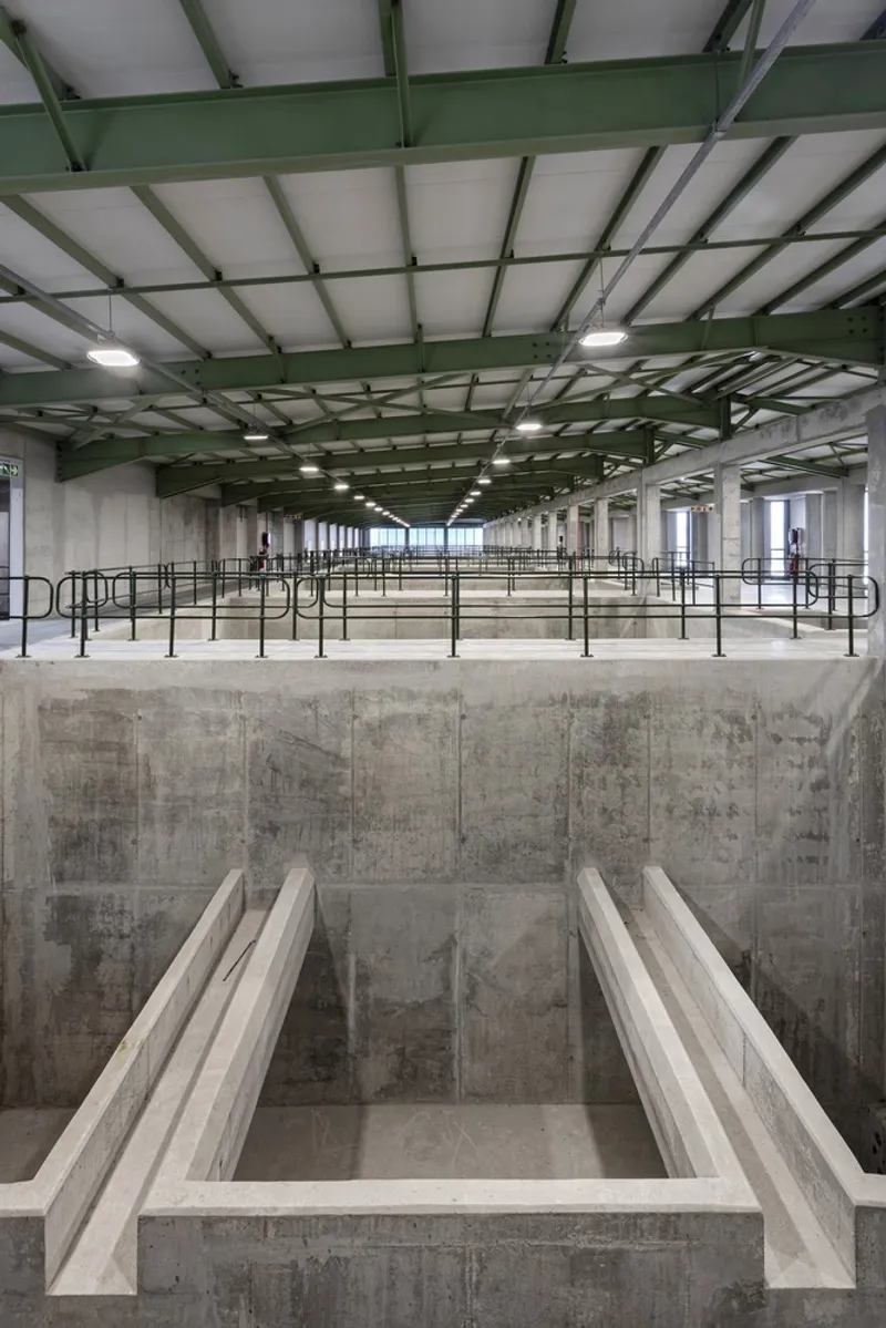 Concrete water channel beneath green painted steel roof structure and mezzanine railings