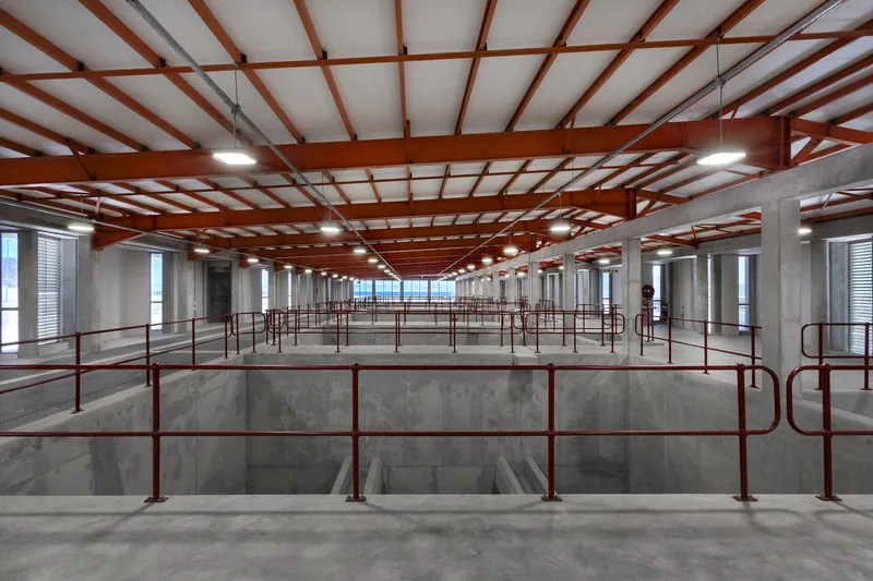 Concrete basins with red metal railings under red steel roof beams and white infill panels