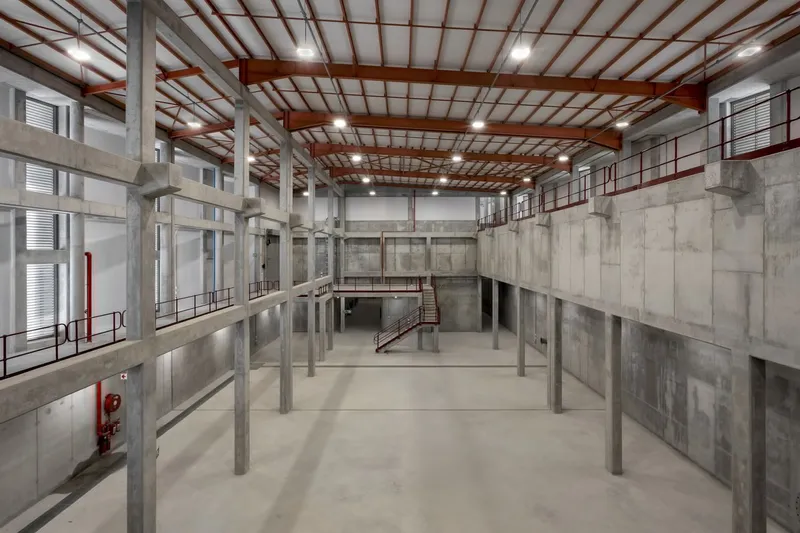Double-height industrial interior with exposed steel columns, concrete walls and timber truss roof structure