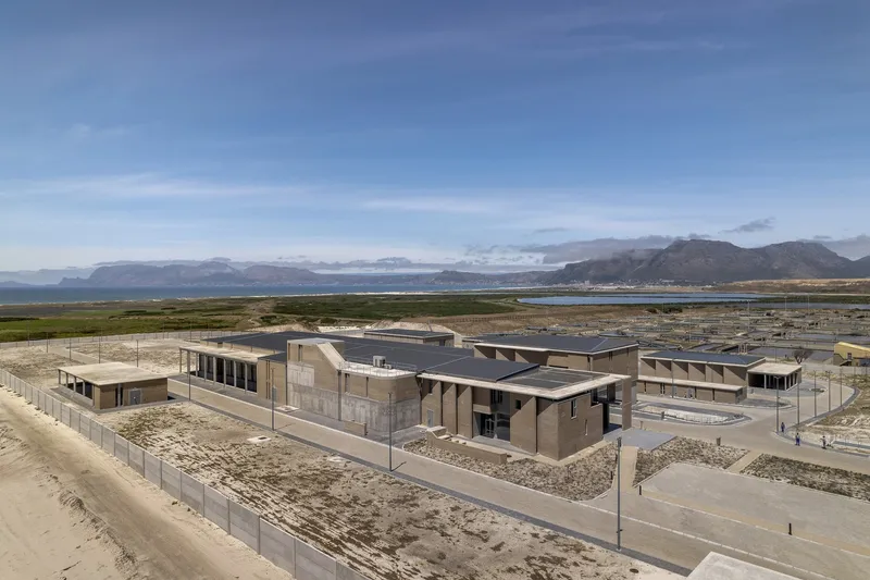 Aerial view of low-rise compound with metal roofs surrounded by coastal wetlands and mountain ranges