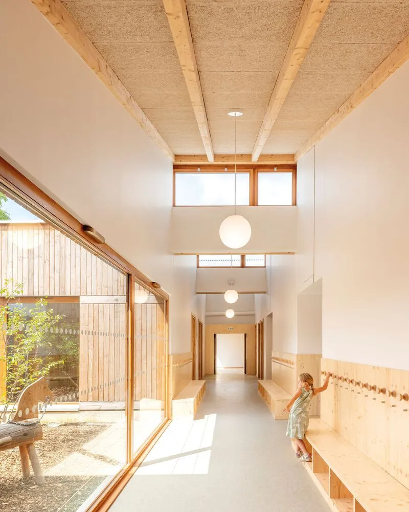 Corridor with exposed timber ceiling beams and full-height glazing overlooking the courtyard with a child walking