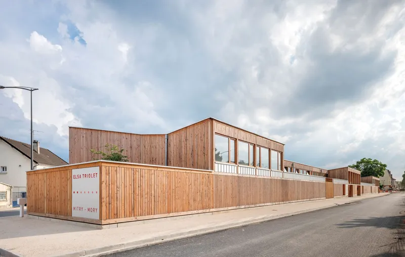 Street view of the vertical timber cladding facade with clerestory windows under a cloudy sky