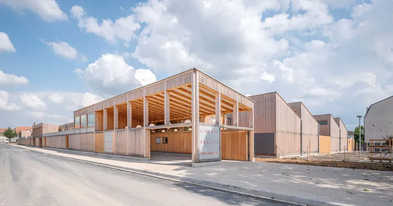 Corner view showing the timber-clad volume with exposed glulam roof structure under afternoon clouds