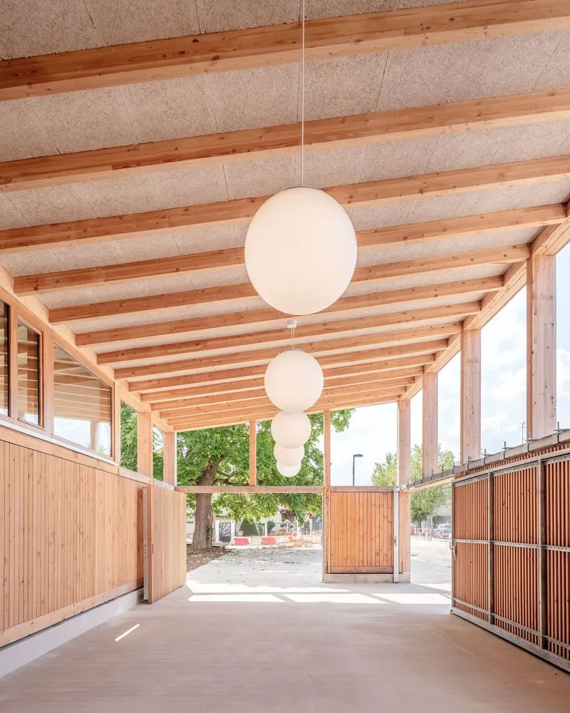 Covered walkway with exposed timber rafters, hempcrete ceiling panels, and spherical pendant lights
