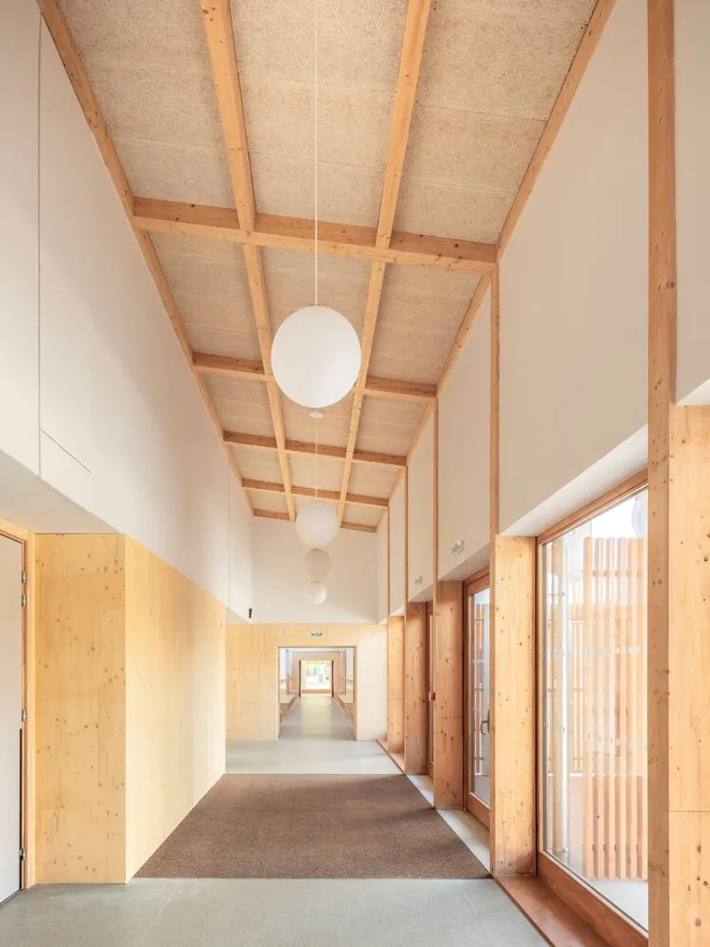 Interior corridor with exposed timber beams and hempcrete ceiling panels above pendant globe lights