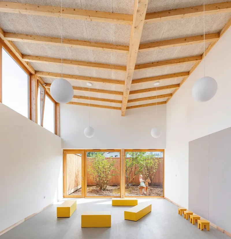 Classroom with yellow foam seating blocks overlooking a gravel courtyard through timber-framed windows