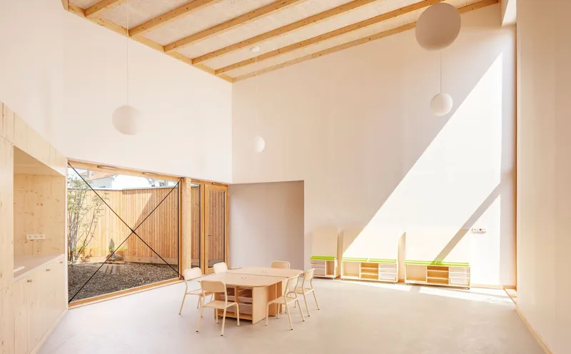 Double-height room with timber table and chairs bathed in angled afternoon sunlight