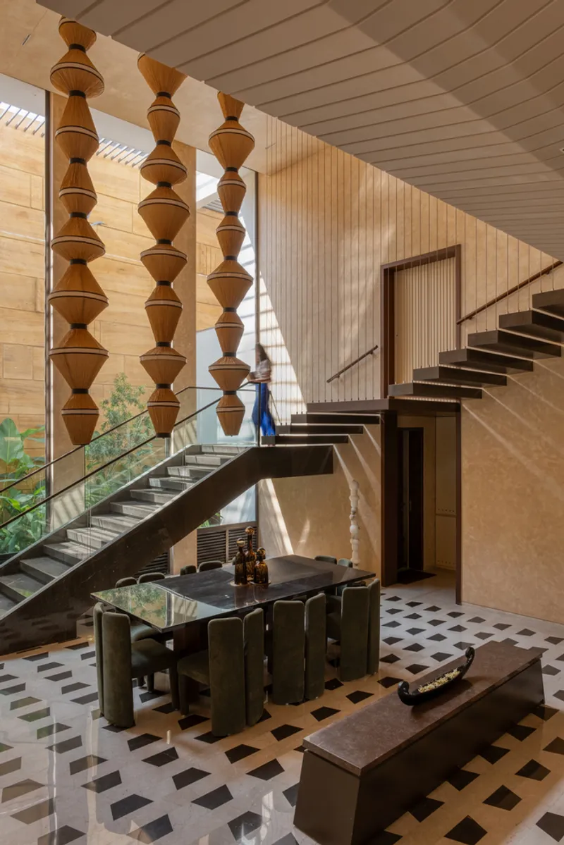 Double-height space with stacked timber ornaments beside a cantilevered staircase and geometric tiled floor