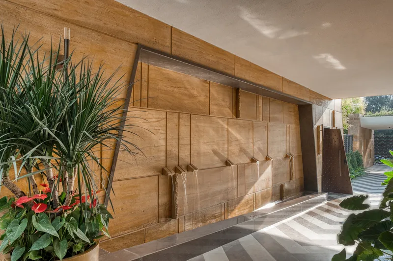 Entry wall clad in geometric sandstone panels with recessed lighting and potted tropical plants