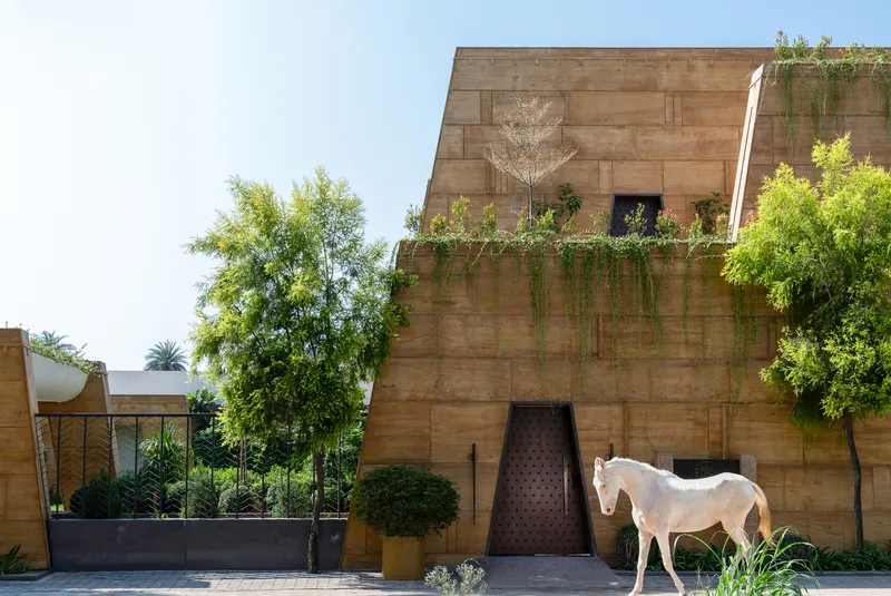 Rammed earth facade with cascading greenery and a white horse standing in the entry courtyard