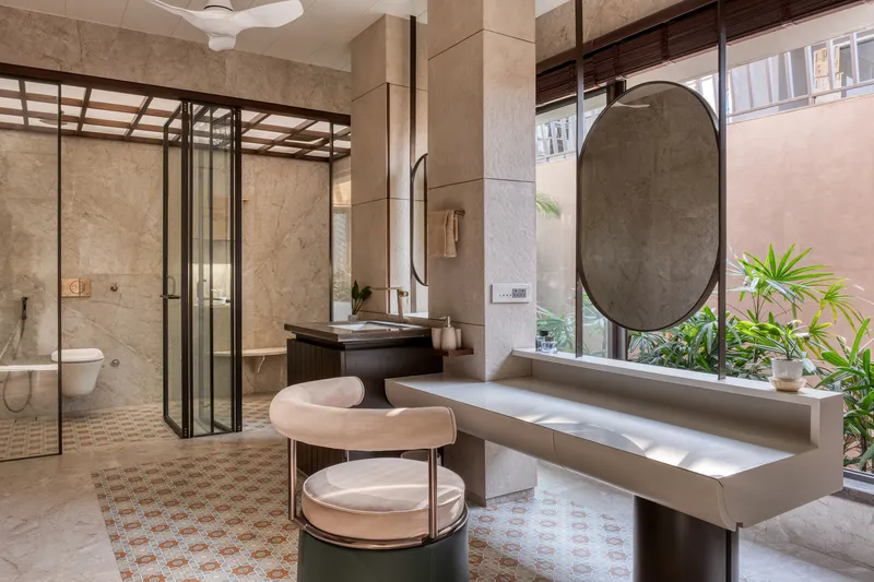 Bathroom vanity with a circular mirror, stone bench and glazed courtyard view with potted palms