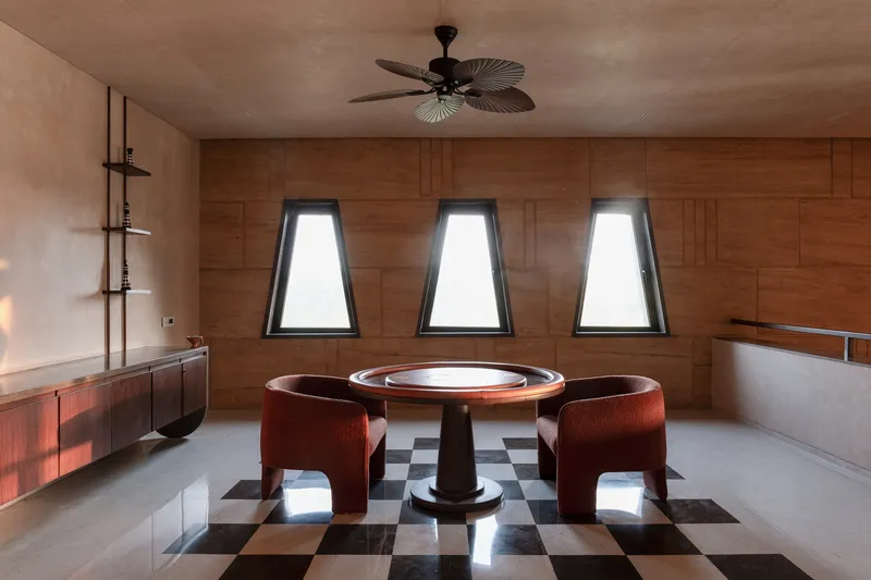 Dining room with patterned wood wall, three trapezoidal windows, and black-and-white chequered floor in soft daylight