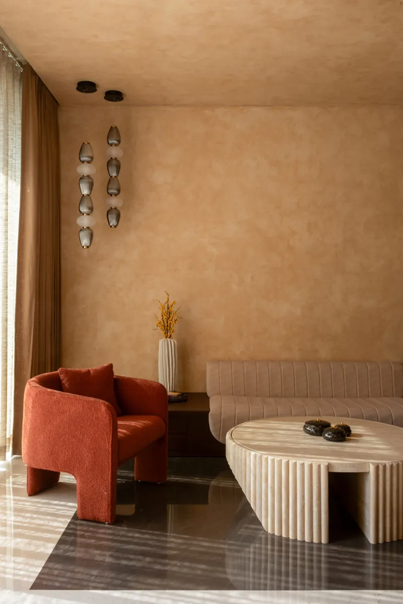 Living room with terracotta armchair, tufted sofa, and fluted coffee table beneath hanging wall sconces
