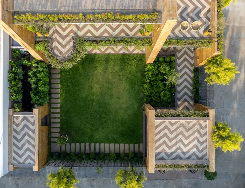 Aerial view of courtyard with central lawn, chevron patterned paving, timber pergola, and planted beds