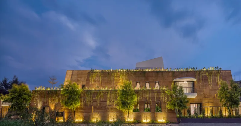 Street facade showing the layered rammed earth walls with planted terraces under a twilight sky