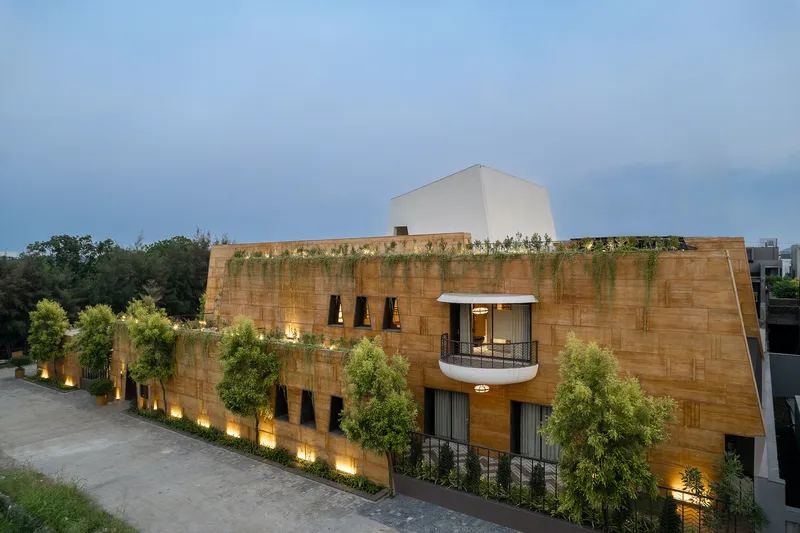 Oblique view of the rammed earth facade with cascading greenery and uplighting at dusk