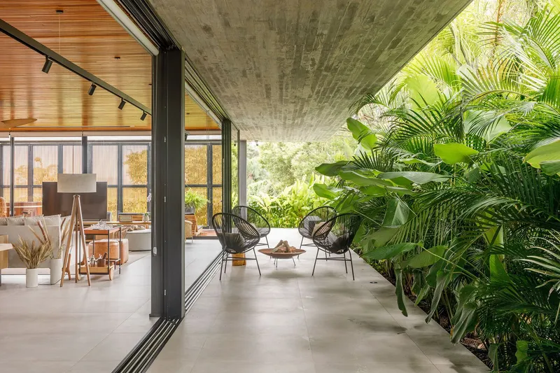 Semi-open living space with sliding glass walls connecting interior seating to terrace bordered by tropical plants