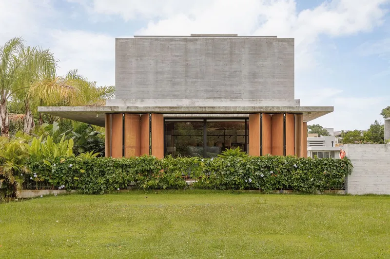 Front facade with board-formed concrete volume above timber-clad ground floor and manicured hedge