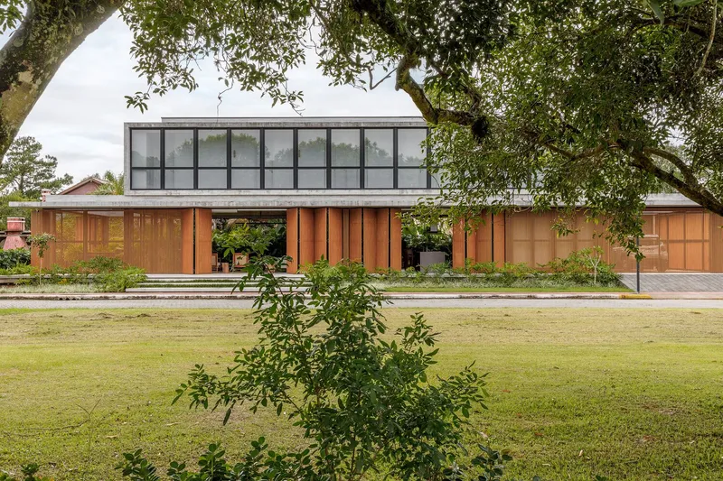 Garden view showing the glazed upper volume and timber facade beneath overhanging tree branches
