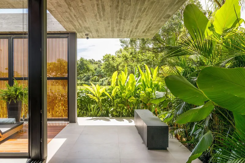Covered outdoor terrace with concrete bench and tropical foliage under board-formed concrete ceiling