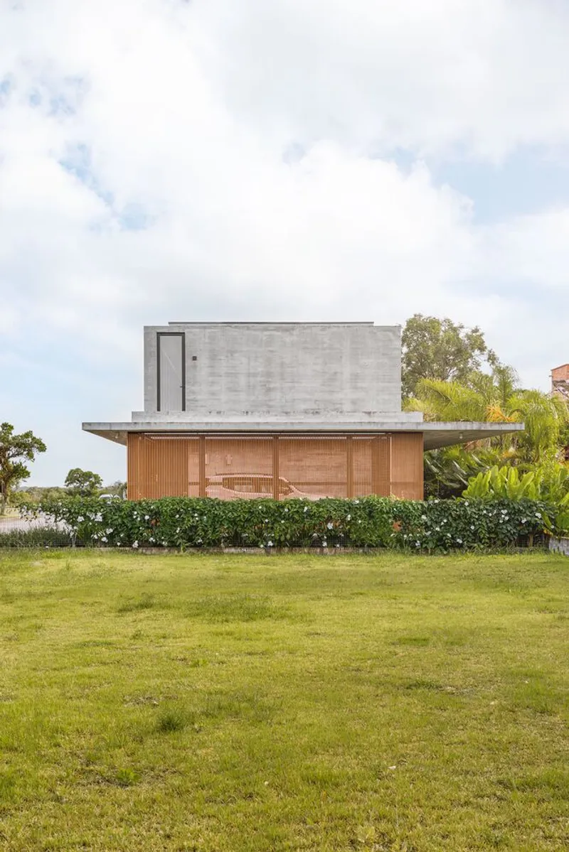 Side elevation showing concrete upper volume cantilevered over timber-clad base with lawn foreground