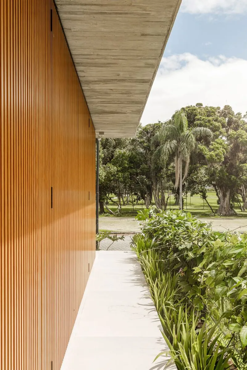 Covered walkway with vertical timber cladding and exposed concrete soffit overlooking a planted bed and lawn