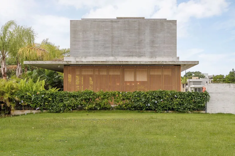 Stacked concrete volume above timber-clad lower level with landscaped hedge and palm trees