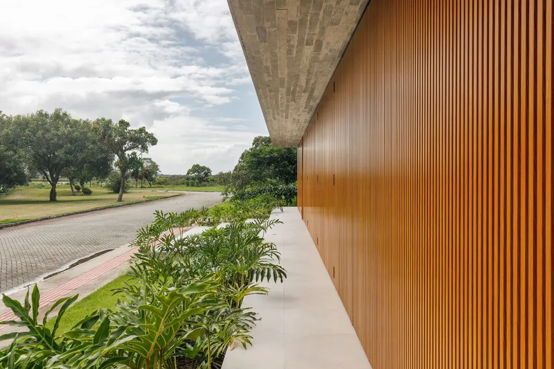 Cantilevered concrete overhang with timber wall and low planting along a paved access road