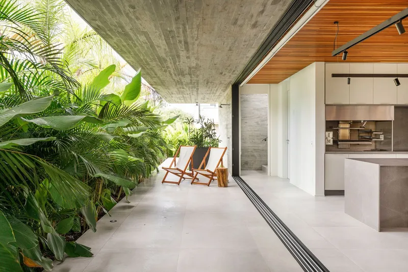 Covered terrace with board-formed concrete soffit opening to planted bed with palms and folding chairs