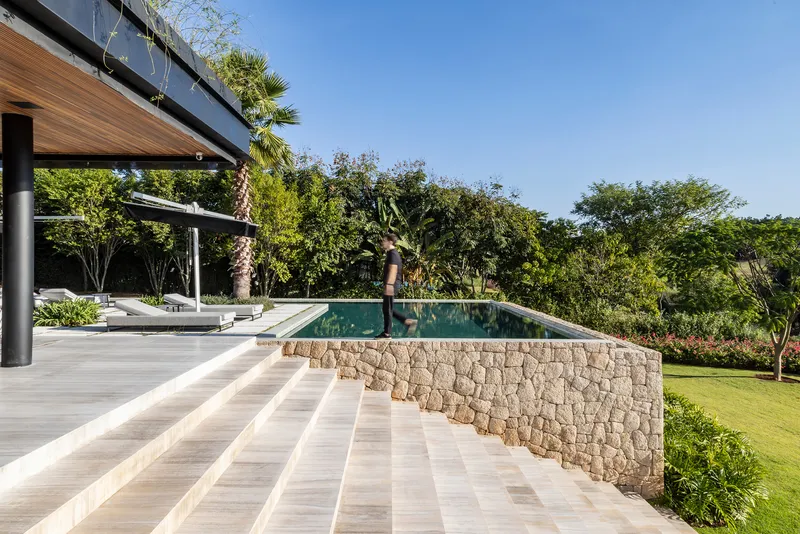 Infinity pool edge with stacked stone retaining wall extending from the timber-decked terrace