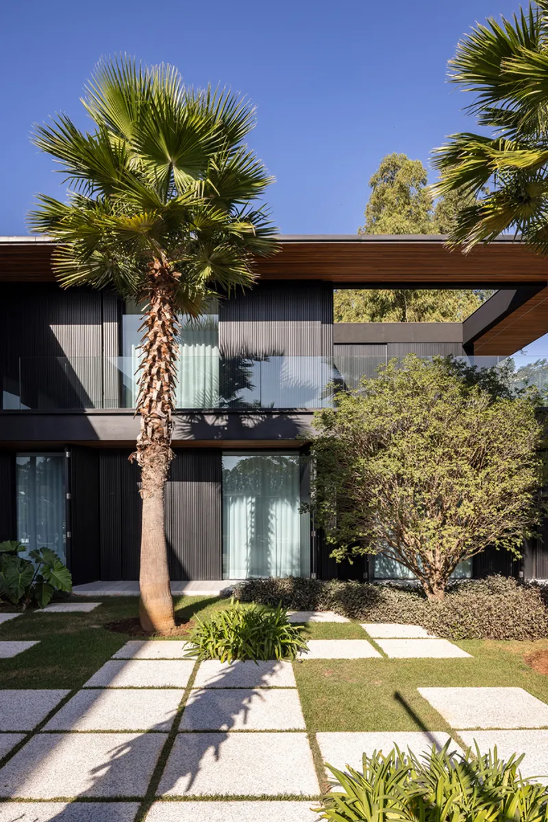 Facade with vertical metal cladding, overhanging timber soffit, and palm tree casting shadows on paved walkway