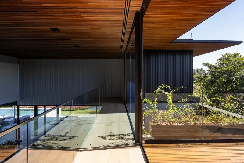 Timber deck terrace with glass balustrade overlooking planted raised beds and distant trees