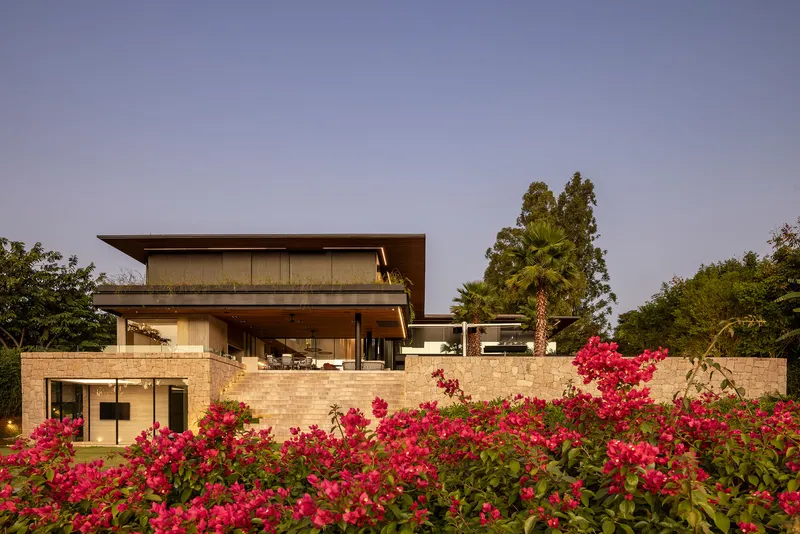Layered stone-clad facade with deep overhangs and flowering shrubs at twilight