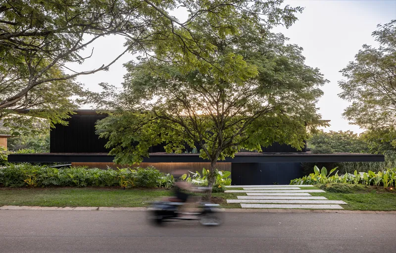 Street facade with black cladding and horizontal bands beneath a canopy of trees as cyclist passes