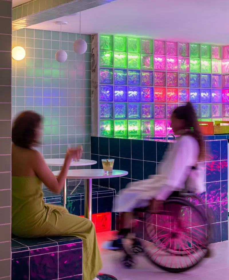 Interior cafe area with backlit colored glass block wall and two figures in motion
