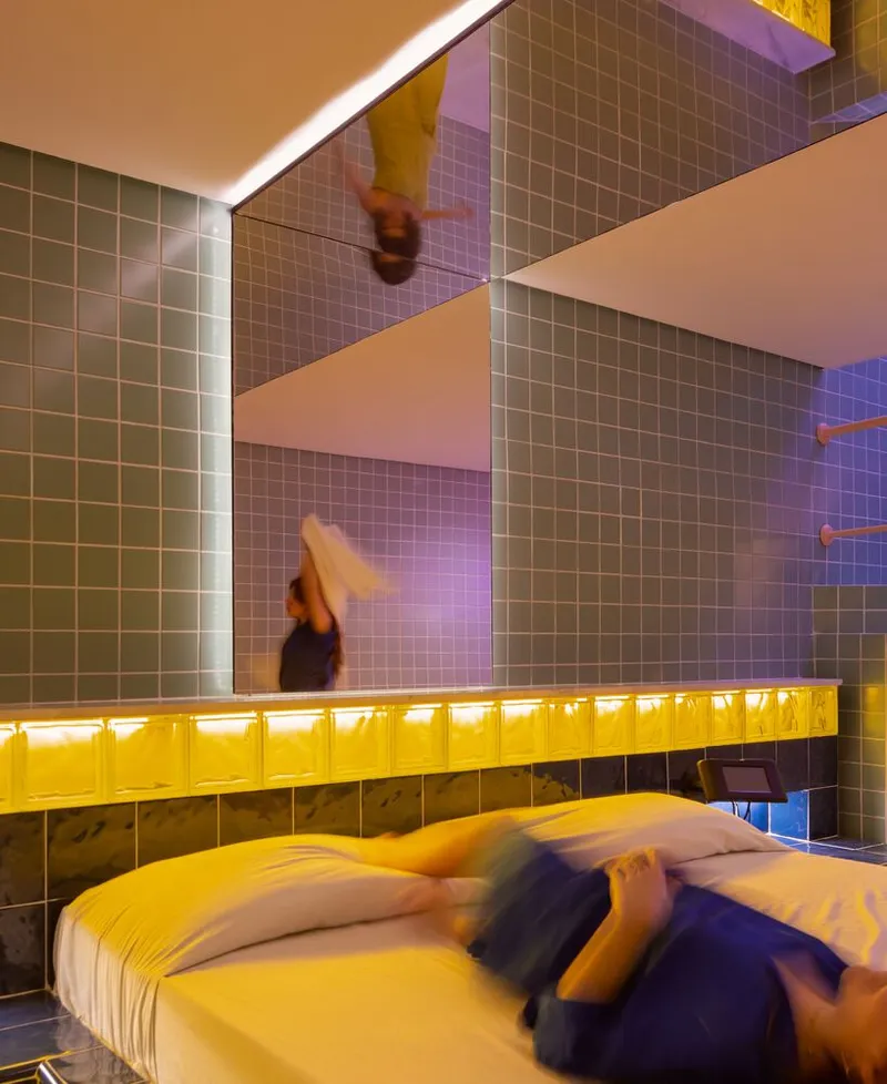 Bedroom with tiled walls and backlit yellow glass block strip above bed with moving figures