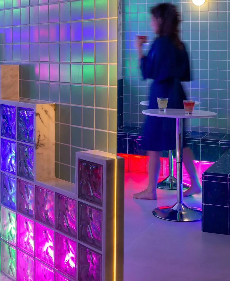 Cafe seating area with illuminated glass block partition and figure passing by pedestal table