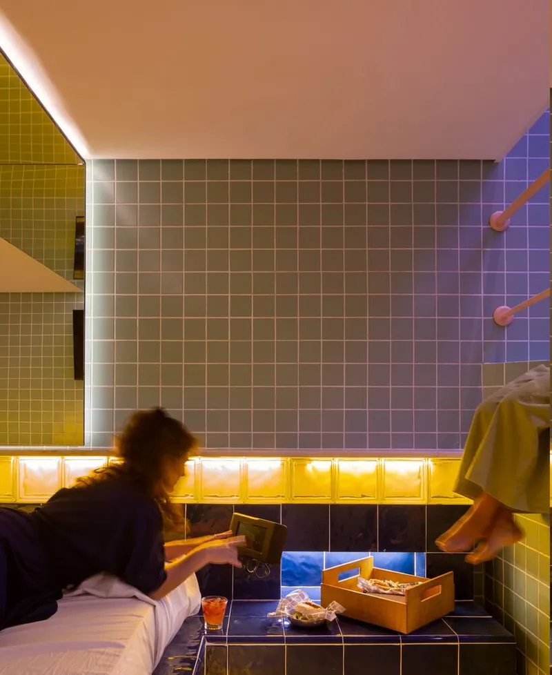 Tiled wall with backlit yellow glass blocks and two people leaning over built-in counter