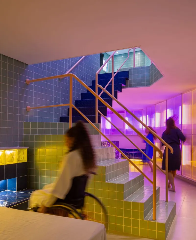 Tiled staircase with pink metal railing ascending past yellow and blue glazed walls under purple light