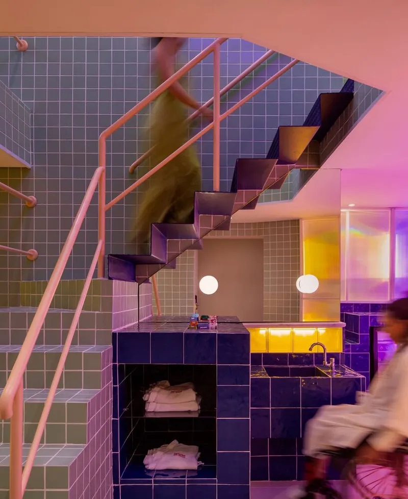 Staircase with pink metal railings rising above a tiled kitchen counter with a blurred figure passing