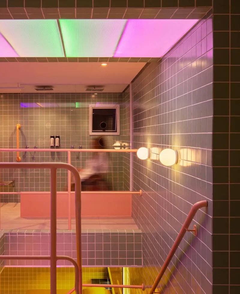 View through pink railings to a tiled bathing platform with globe lights and colored ceiling glow