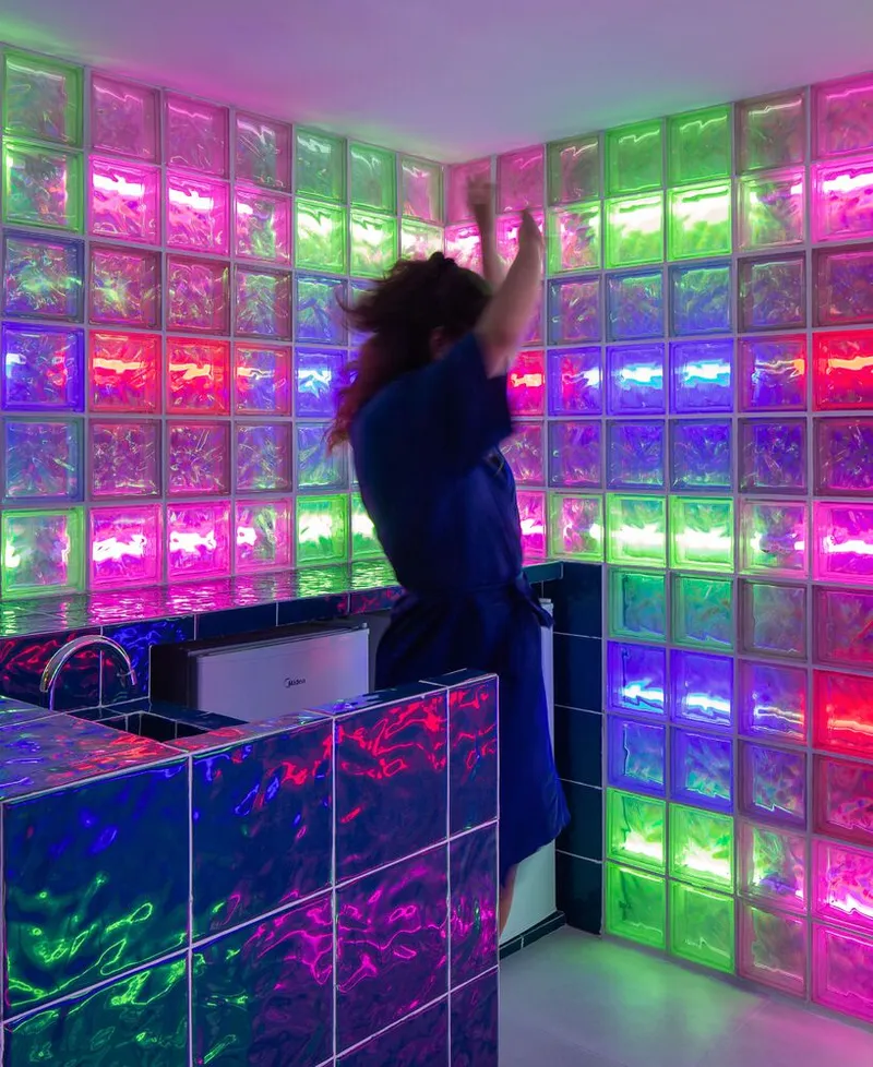 Backlit glass block wall in green, pink, and purple hues with a figure in motion