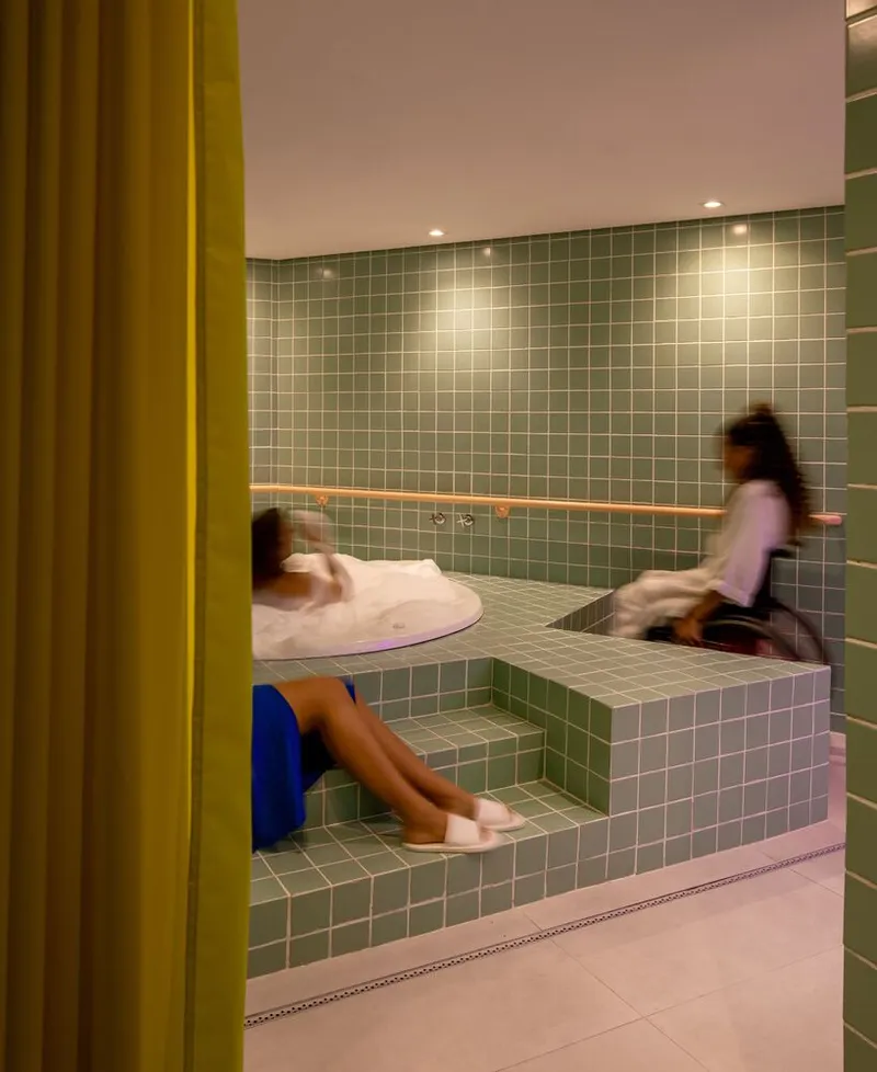 Green tiled bathing platform with two figures separated by a yellow curtain at the edge