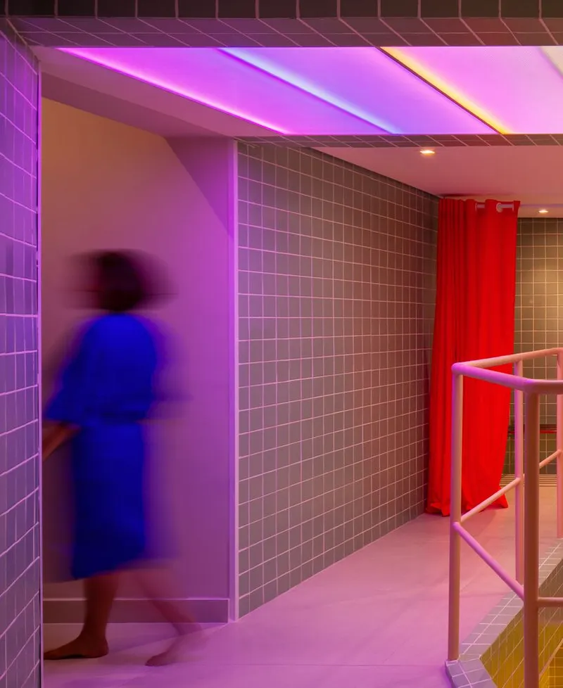 Corridor with square tile walls bathed in pink and purple light with a figure in motion