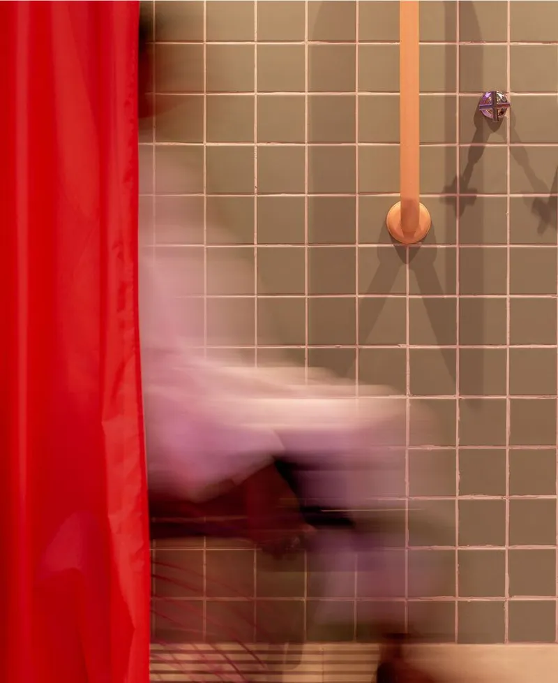 Square tile wall in warm tones with colorful wall-mounted fixtures and a red curtain beside a blurred figure