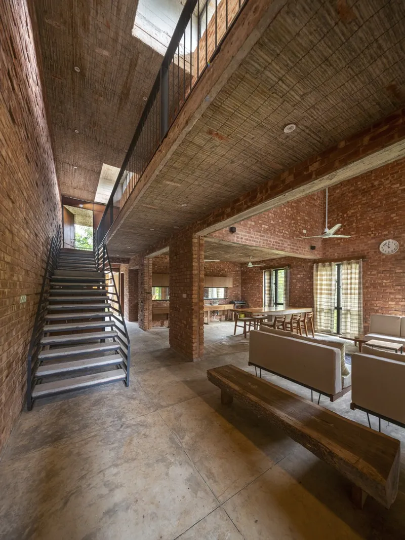 Double-height interior with exposed brick walls, woven bamboo ceiling and steel staircase ascending to clerestory windows